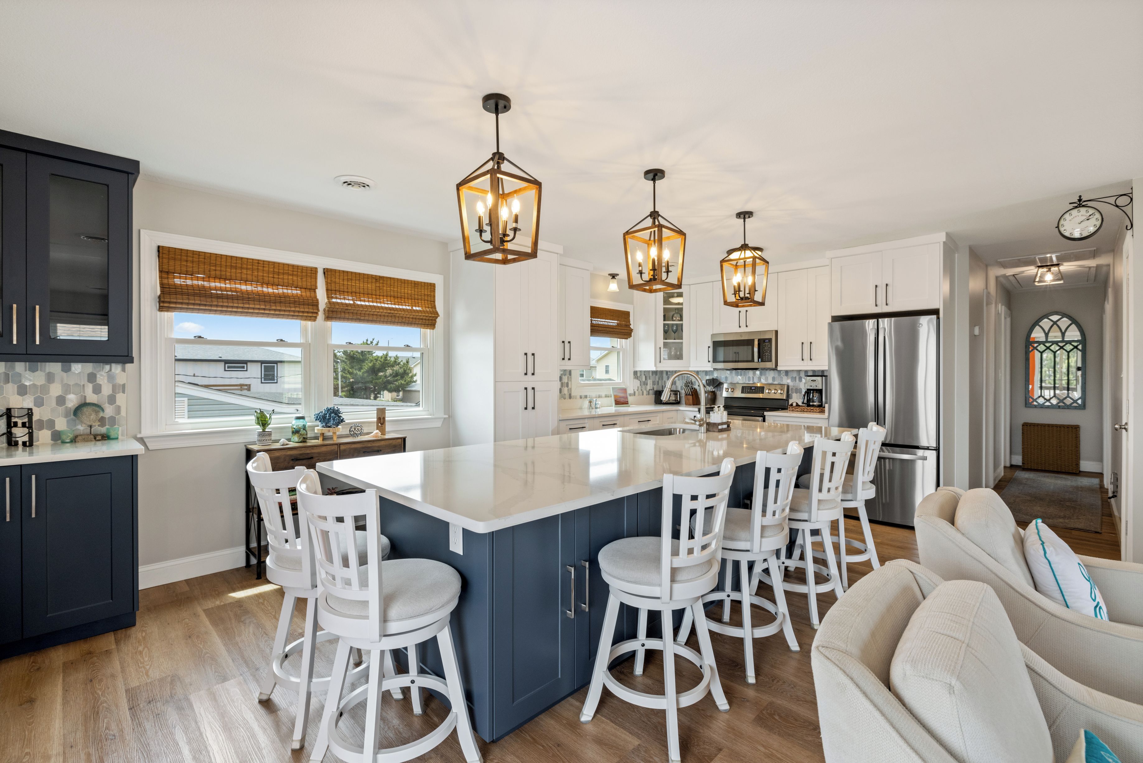 A modern kitchen with a central island, white bar stools, and pendant lighting.