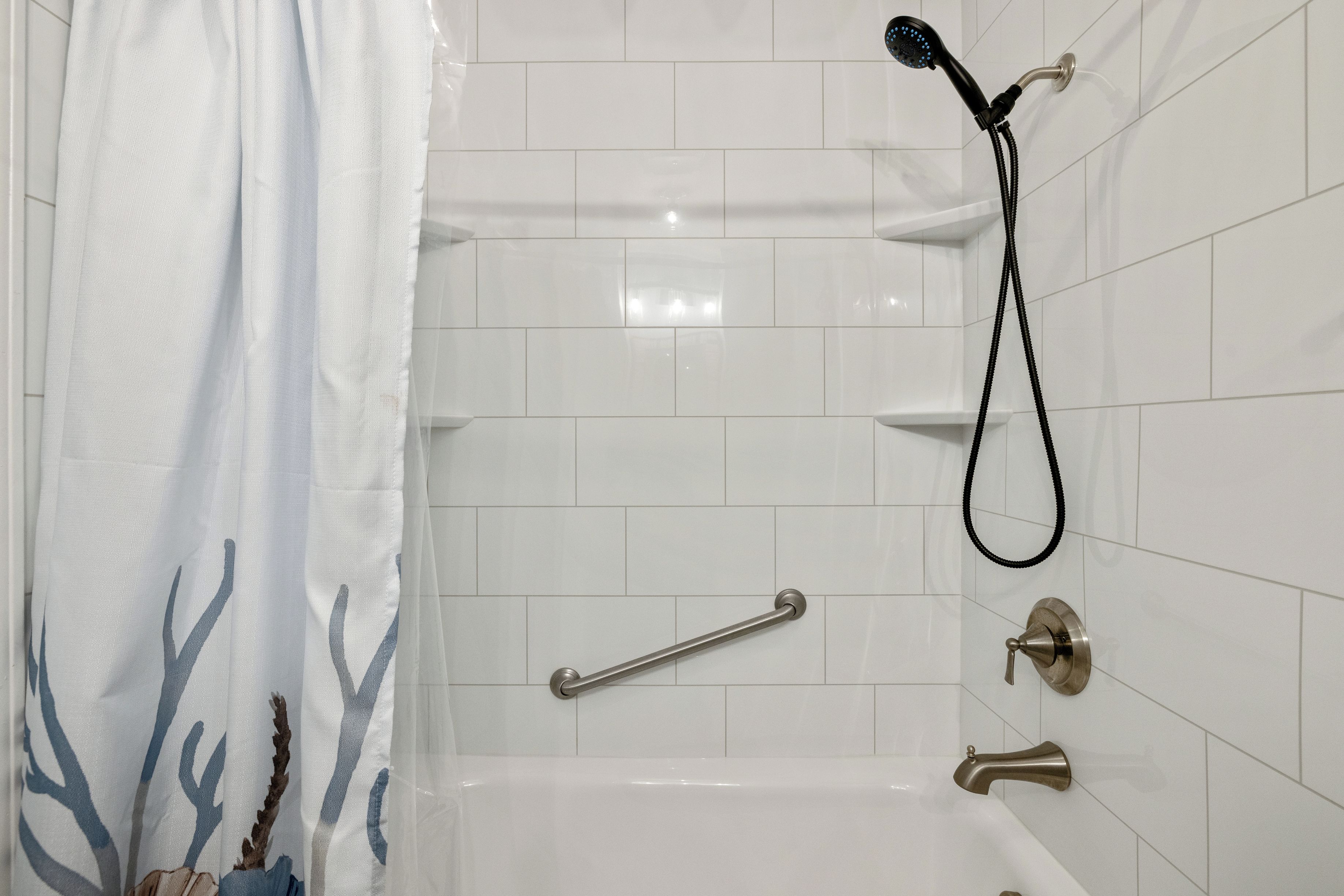A bathroom with white tiled walls, a shower with a handheld showerhead, a grab bar, and a towel rack.