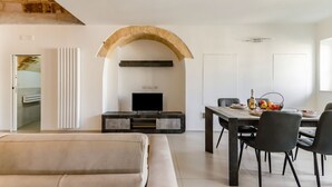 Una sala de estar moderna con sofá, una mesa de comedor con sillas, televisor y un arco de piedra.