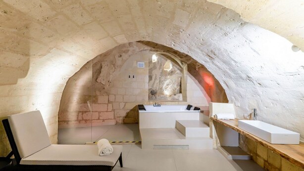 Un cuarto de spa con techo abovedado de piedra, una bañera, un lavamanos, un banco y una toalla.