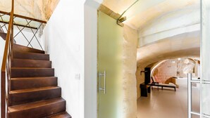 Una escalera de caracol conduce a una habitación con pared de piedra, una bañera y un sillón de descanso.