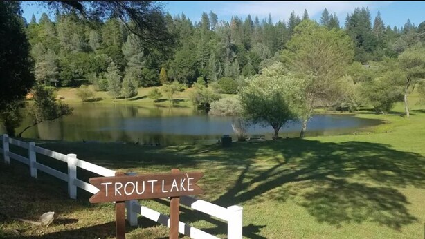 A sign for Trout Lake with a white fence in the foreground.