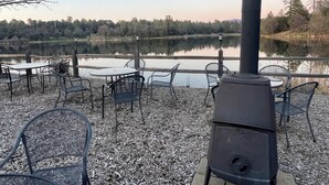 An outdoor seating area with tables and chairs facing a lake, a chimney, and a lamp post.
