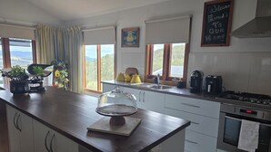 A modern kitchen with a large island, a stove, and a sink. There are potted plants on the counter and a chalkboard with a welcome message.