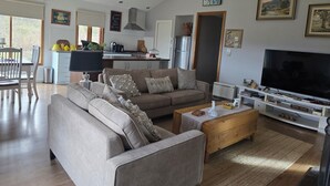 A modern living room with a sofa, coffee table, and TV, a kitchen with appliances, and a dining area with chairs.