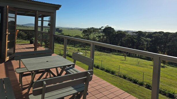 A wooden deck with a table and bench, overlooking a grassy field and distant hills.