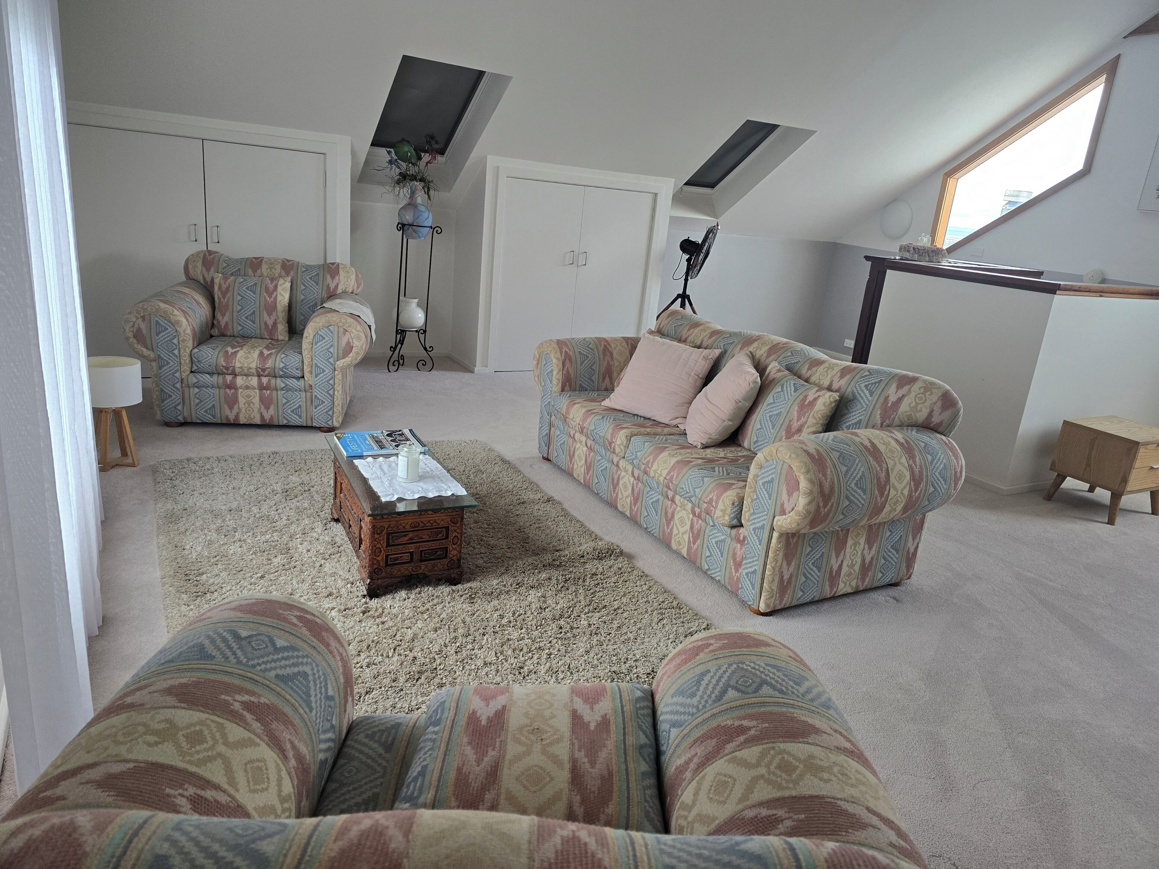 Una sala de estar con sofás estampados, una mesa de centro, un televisor y un ventilador.