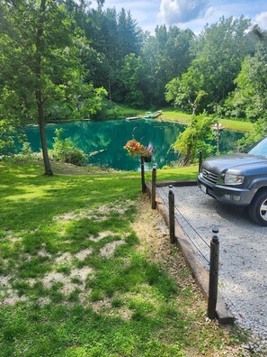 Un chemin de gravier mène à une étendue d’eau verdoyante où est amarré un bateau, le tout étant entouré d’une végétation luxuriante et d’arbres.