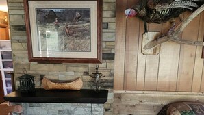 A rustic room with a stone fireplace, a framed picture above it, a wooden bed, and a mounted turkey.