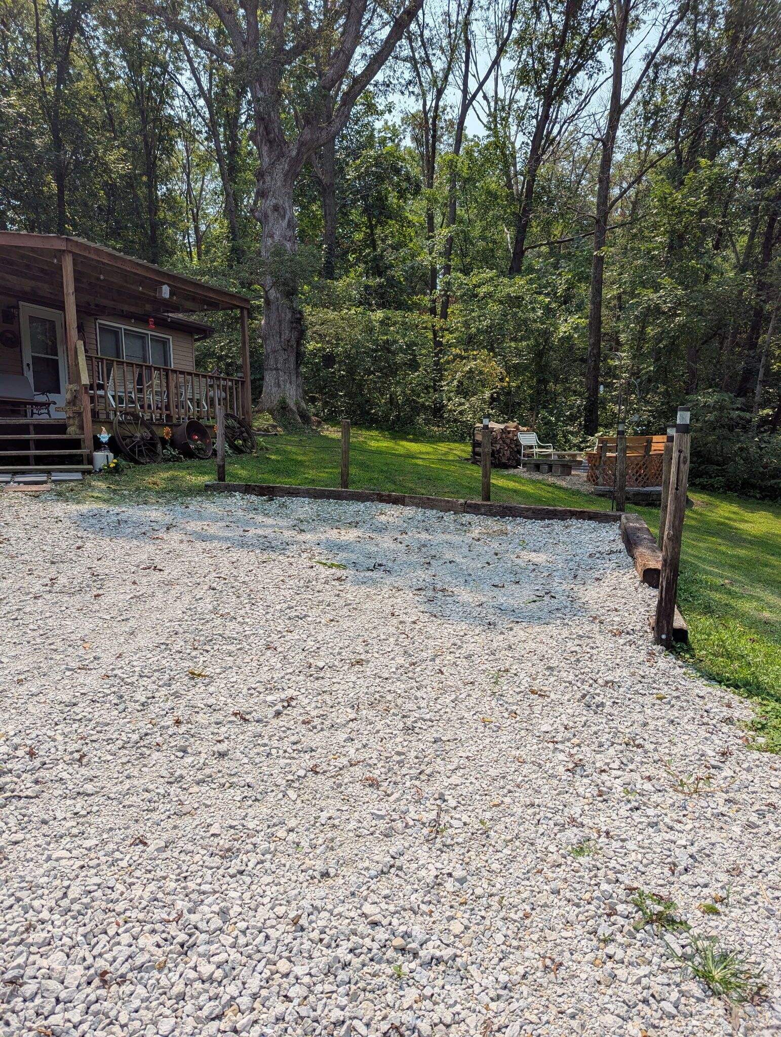 A gravel driveway leading to a wooden cabin with a porch, surrounded by trees and a grassy area.
