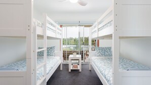 Un dormitorio con literas, una pequeña mesa con libros y vistas al exterior a zonas verdes.