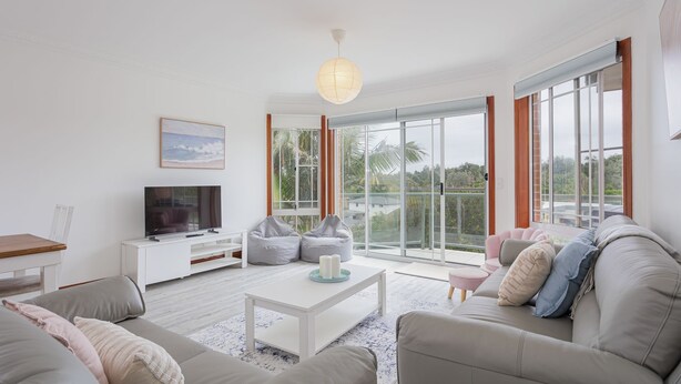 Una sala de estar moderna con un televisor de pantalla plana, asientos cómodos y ventanas amplias con vistas a la vegetación.