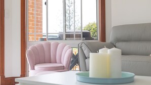 Una sala de estar acogedora con un sillón rosa, un sofá gris y una mesa blanca con una bandeja azul.