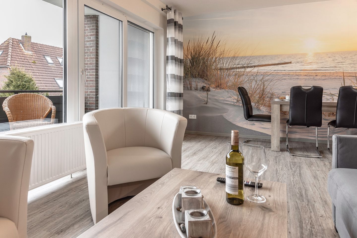 Un salon moderne doté d’une grande fenêtre, d’un canapé incurvé, d’une table à manger avec des verres à vin et d’une fresque murale représentant une scène de plage.