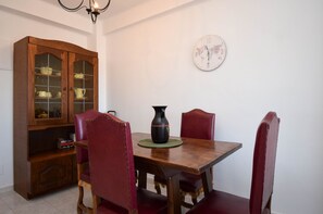 Une salle à manger avec une table en bois, quatre chaises à revêtement rouge, un buffet en bois avec des portes en verre et une horloge murale.