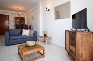 Un salon avec un canapé bleu, une table basse en bois et un téléviseur posé sur un meuble en bois.
