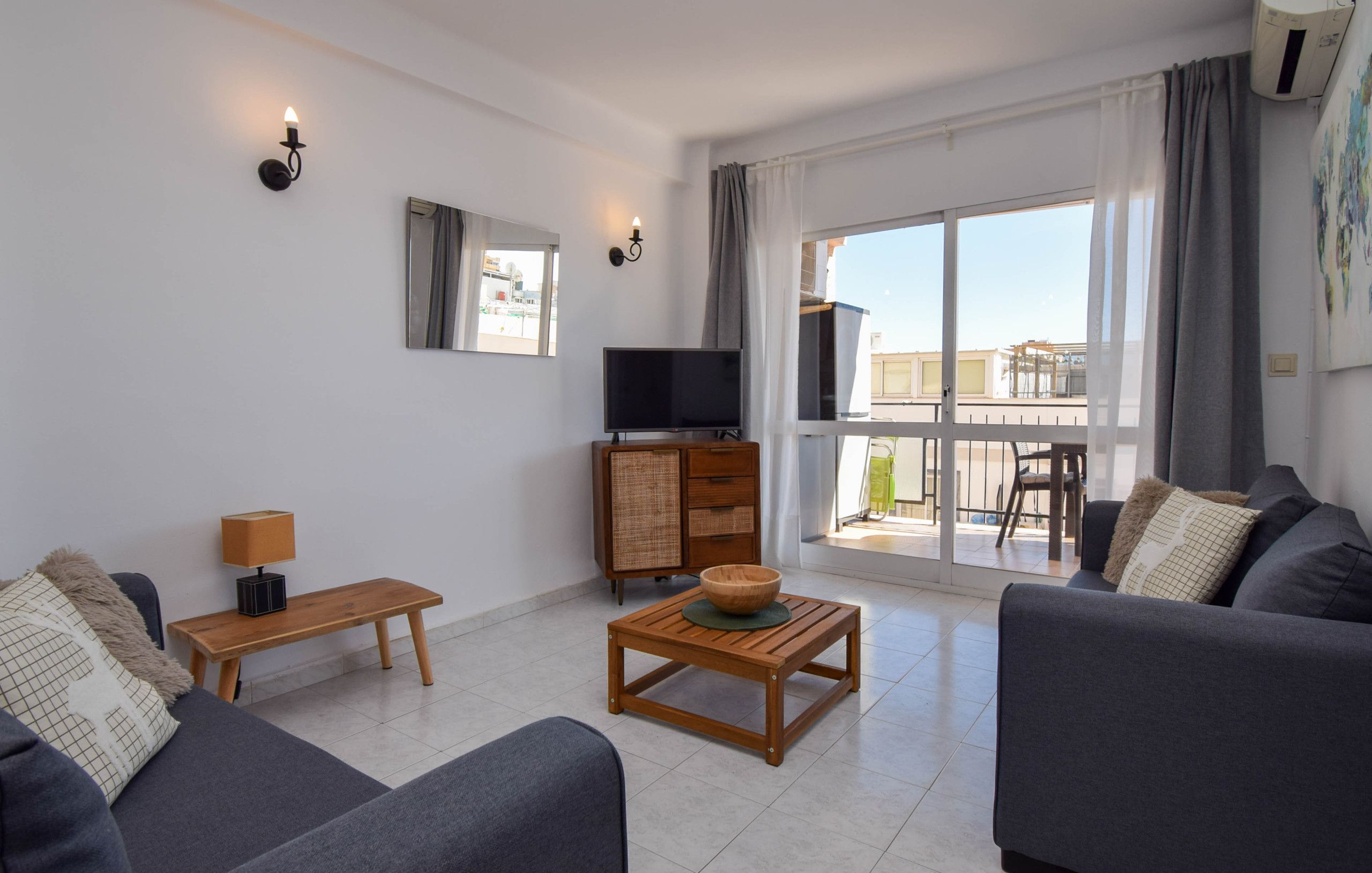 A modern living room with a sofa, a wooden coffee table, a TV, and a balcony with a view.