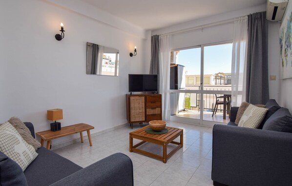 A modern living room with a sofa, a wooden coffee table, a TV, and a balcony with a view.