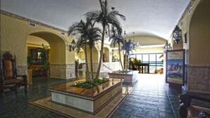 Eine Lobby mit einem zentralen Blumentopf, Palmen und Blick auf den Ozean durch große Fenster.