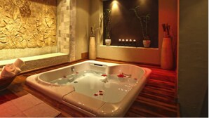 Ein Spa-Zimmer mit einer großen Badewanne, einer Steinwand und einem Fenster mit Pflanzen.