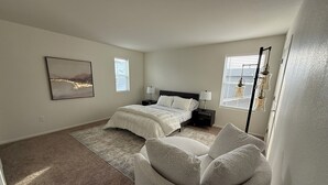 Een slaapkamer met een bed, nachtkastjes, een stoel en een schilderij aan de muur.