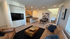 Een moderne woonkamer met een grote flatscreen televisie, een bruine leren bank, een houten salontafel en een zwart tapijt.