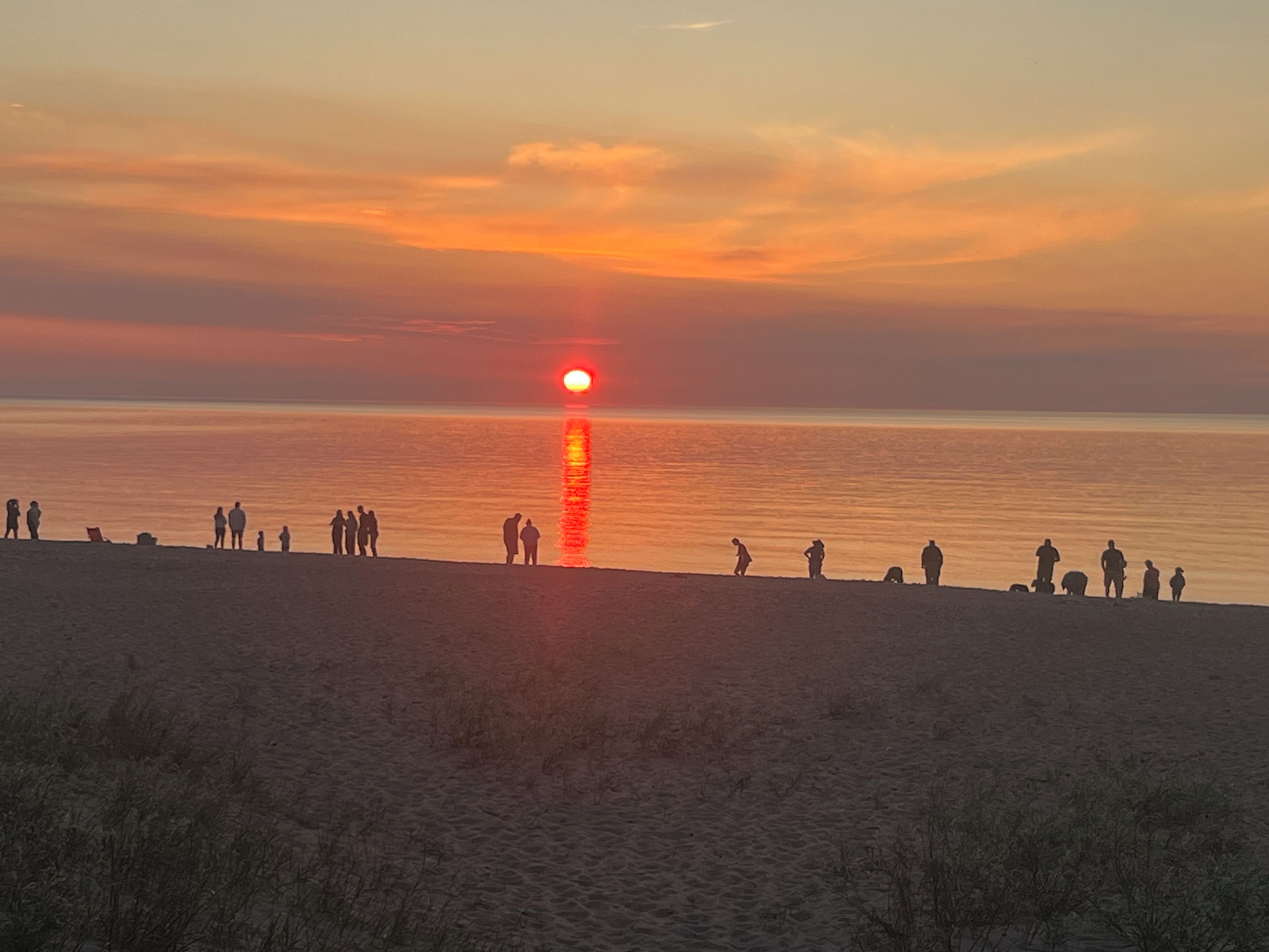 Solnedgang over en strand med silhuetter af mennesker mod himlen.