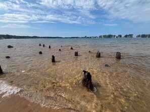 Ein Strand mit klarem Wasser und versunkenen Holzpfählen.