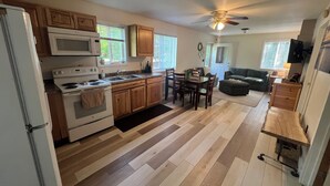 Una cocina con armarios de madera, microondas y estufa. Hay un comedor con mesa y sillas.