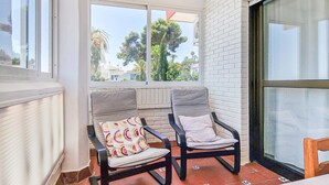 A balcony with two chairs, a window with a view of trees, and a white brick wall. - Nice apartment in Malaga with swimming pool (Malaga)