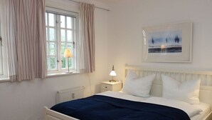 A bedroom with a bed, a bedside table with a lamp, a window with curtains, and a framed picture on the wall. - Vacation at Hüs Dikstian in Alkersum - Hüs Dikstian (Alkersum)