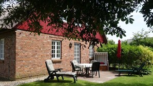 A brick house with a red roof, a patio with a table and chairs, and a red umbrella. - Vacation at Hüs Dikstian in Alkersum - Hüs Dikstian (Alkersum)
