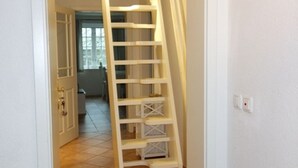 A white interior with a wooden ladder leading to a door.