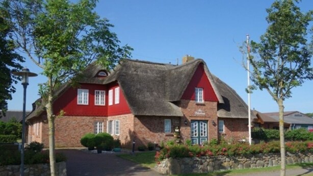 A red brick house with a thatched roof and a stone pathway leading to the entrance.