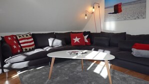 A modern living room with a sectional sofa, a white coffee table, and a beach-themed painting on the wall.