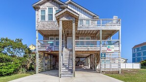 A multi-story wooden building with a balcony, a basketball hoop, and a sign indicating 'Siren's Serenade'. - 4 br Ocean view, beach, pool! (Rodanthe)