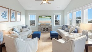 A spacious living room with a large TV, two sofas, a coffee table, and a ceiling fan. - 4 br Ocean view, beach, pool! (Rodanthe)