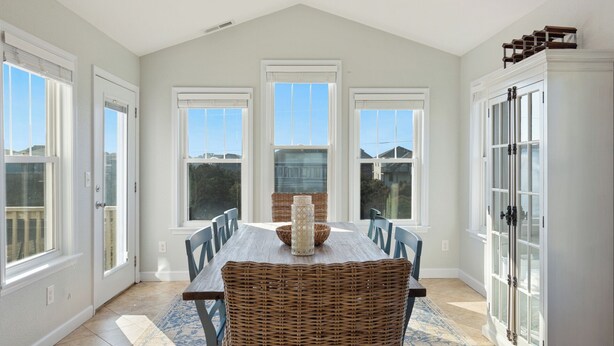 A dining room with a high ceiling, large windows, and a central table with chairs. - 4 br Ocean view, beach, pool! (Rodanthe)