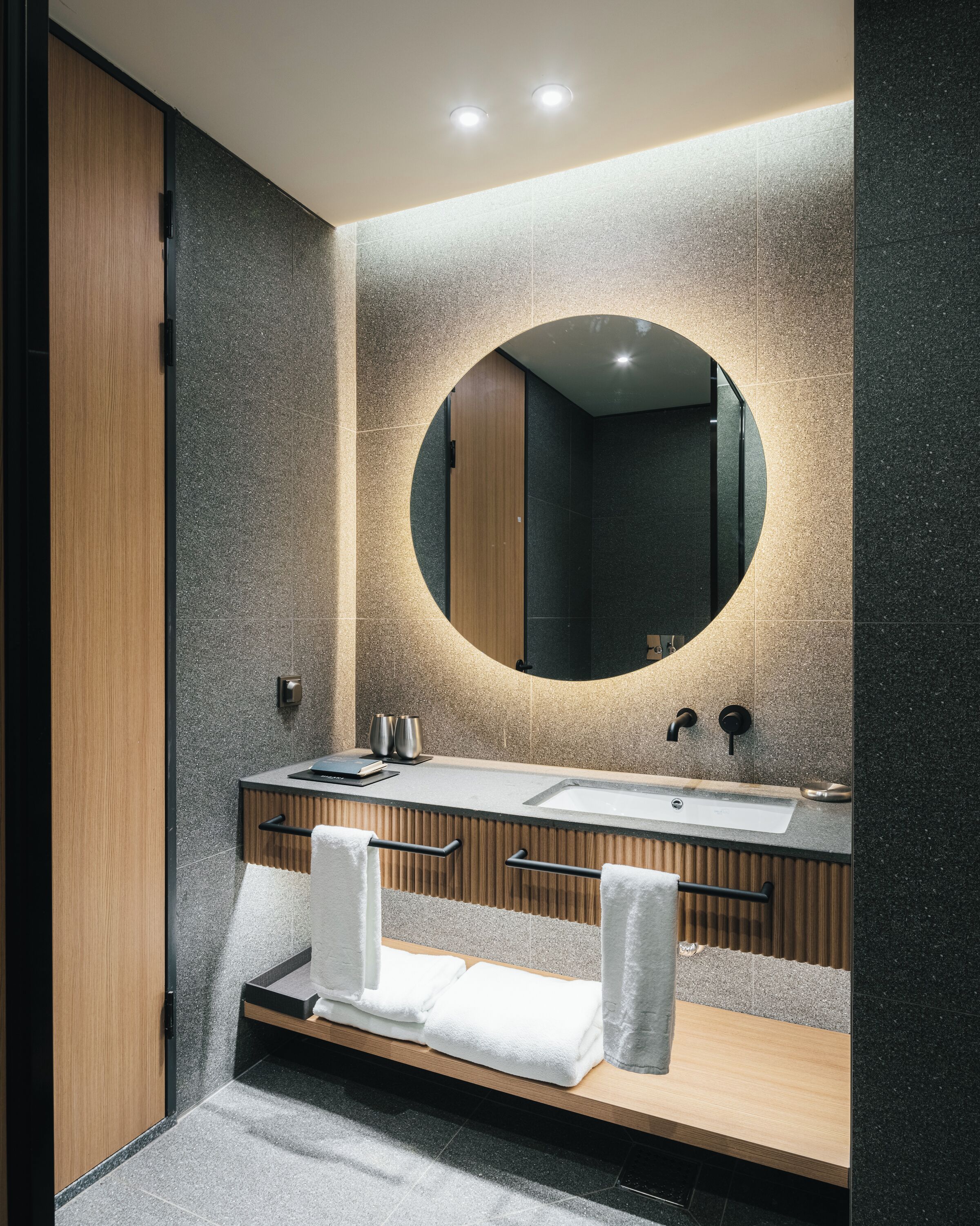 A modern bathroom with a wooden vanity, a large mirror, and a built-in sink.