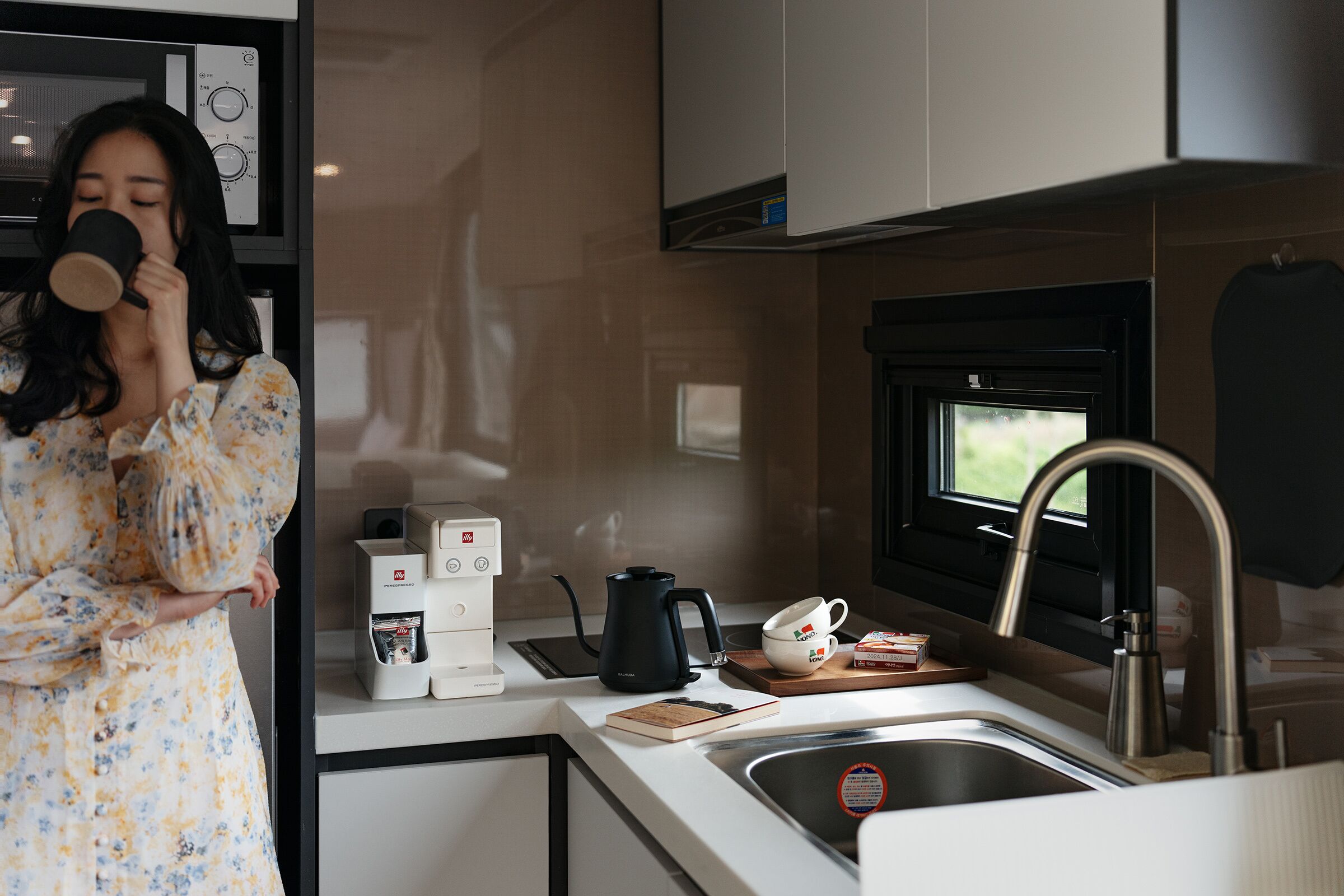 A modern kitchen with a coffee maker, kettle, and a window above the sink.