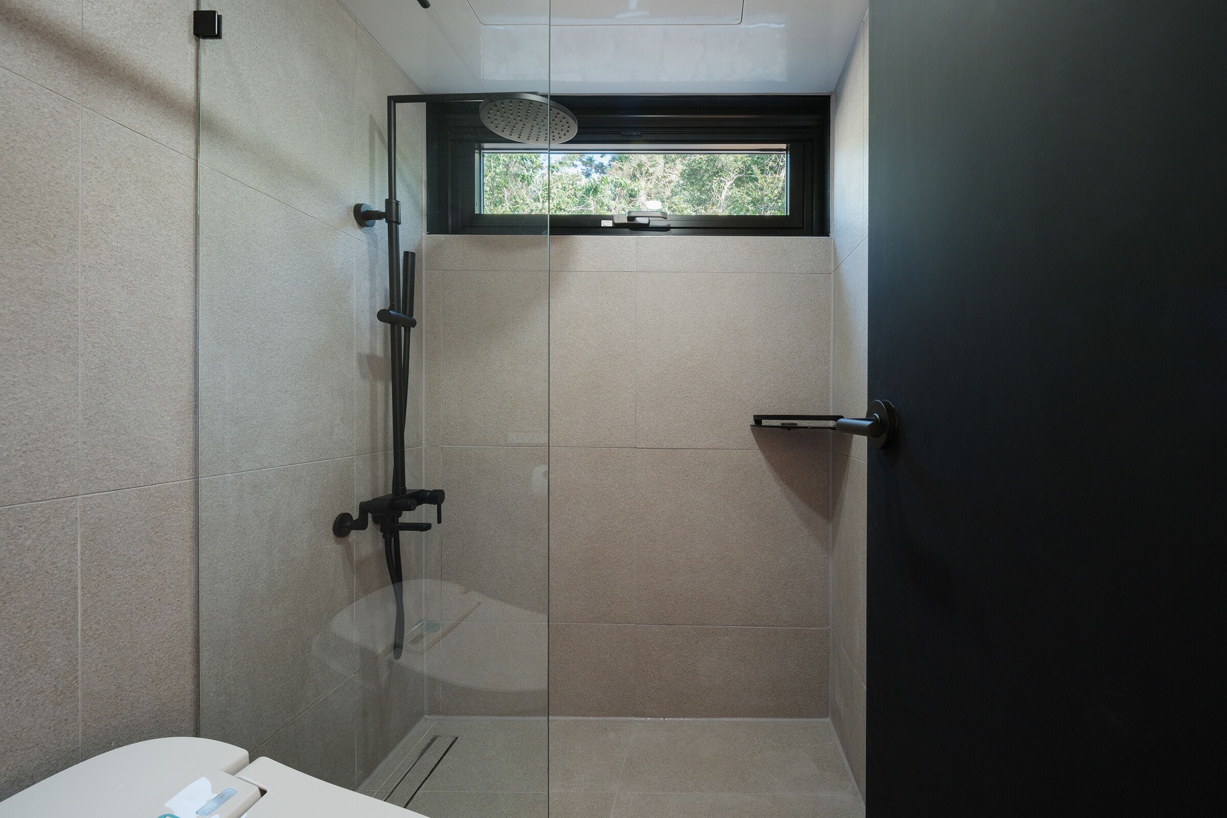 Ein modernes Badezimmer mit Duschkabine aus Glas, Toilette und Fenster mit Blick auf Grünflächen.