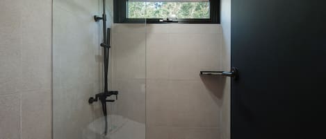 Ein modernes Badezimmer mit Duschkabine aus Glas, Toilette und Fenster mit Blick auf Grünflächen.