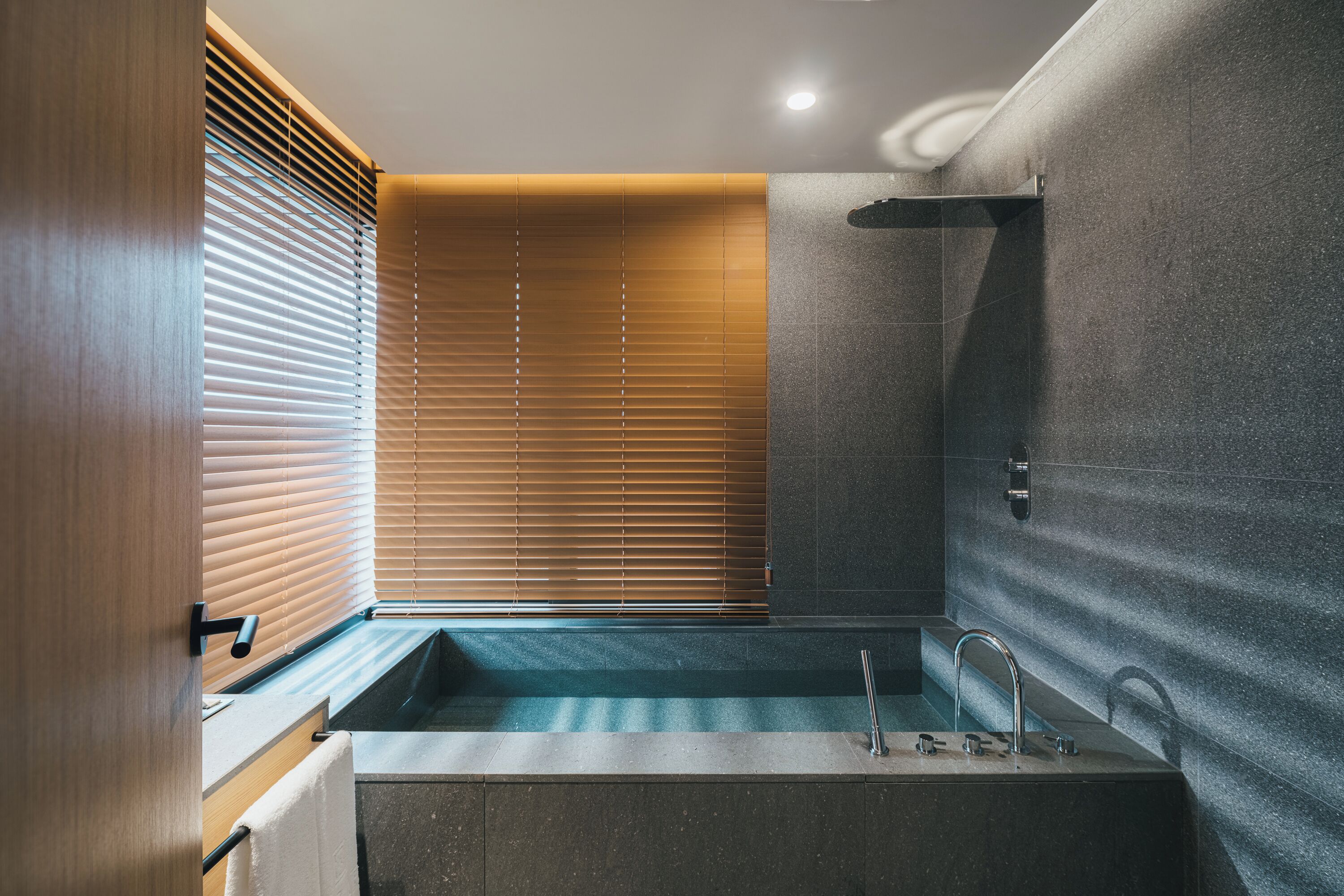 A modern bathroom with a bathtub, a shower, and a window with blinds.