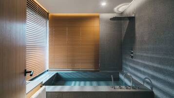 A modern bathroom with a bathtub, a shower, and a window with blinds.