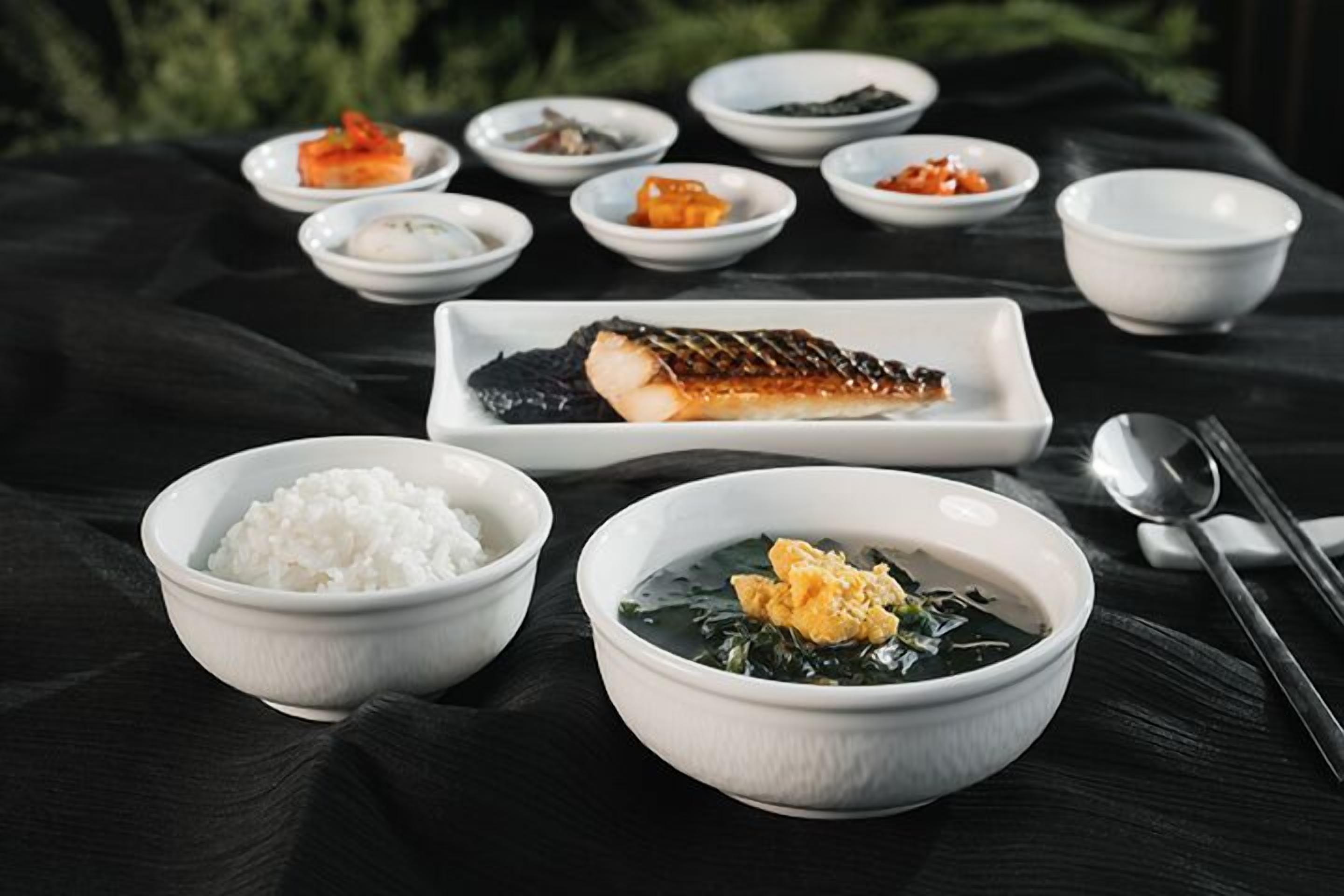 A traditional Korean meal with rice, soup, and various side dishes on a dark tablecloth.