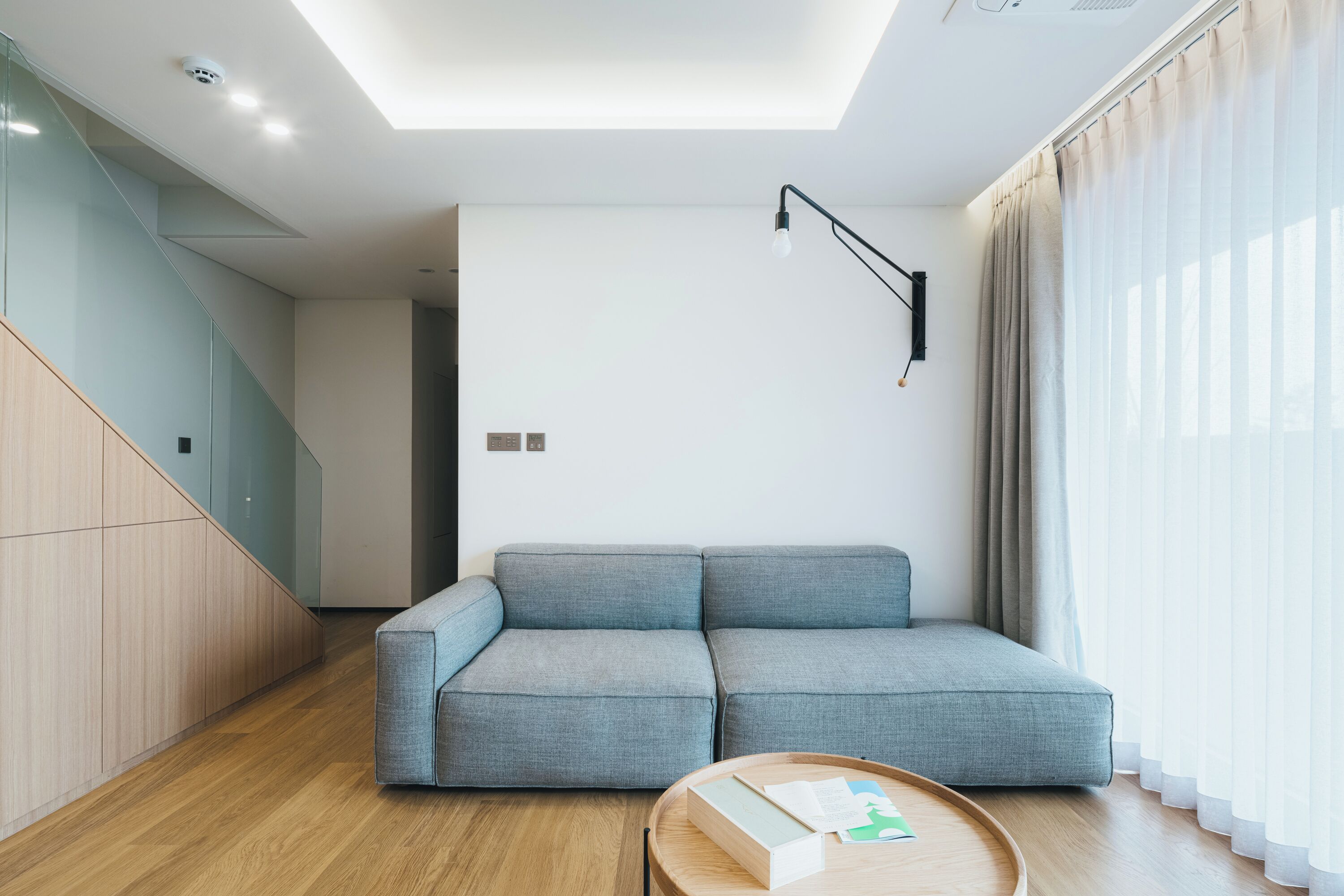 Un salon moderne avec un canapé d’angle gris, une table basse en bois et un luminaire suspendu au plafond.