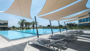 Una piscina con sillas de descanso y toldos de sombra, rodeada de palmeras y edificios modernos.