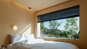 Un dormitorio con un ventanal grande, una cama y una mesita de noche con lámpara.
