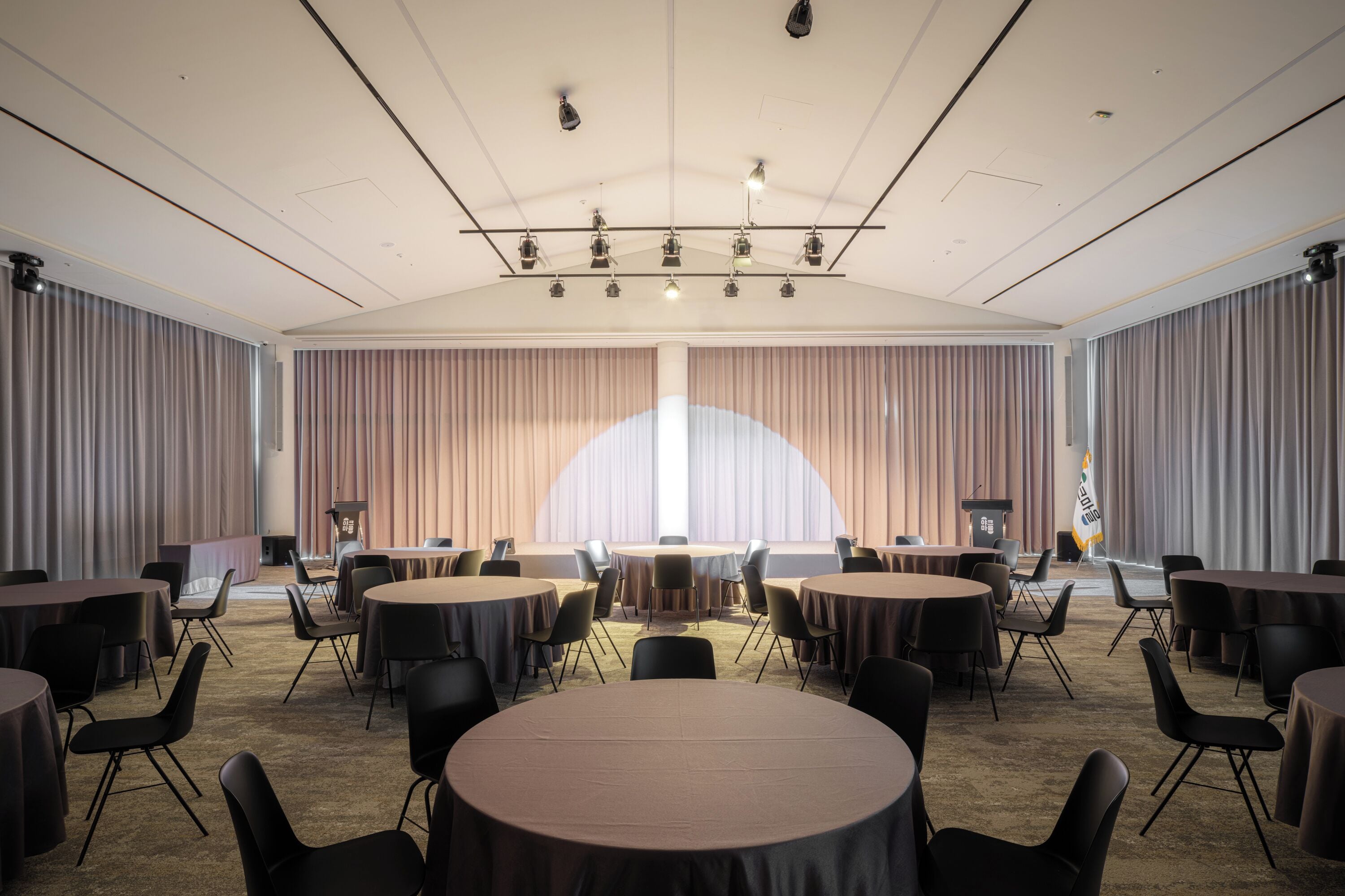 A conference room with round tables and chairs, a podium, and curtains.