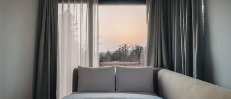 Une chambre d’hôtel avec un grand lit, deux oreillers et une vue sur les arbres à travers de fines rideaux.